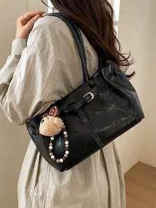 Minimalist black tote bag with plush bear charm worn by a model in a cozy setting