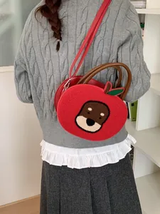 Red apple-shaped crossbody bag with cartoon embroidery and green leaf detail handles