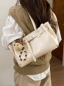 Minimalist beige tote bag with buckle strap and plush bear charm worn by a model