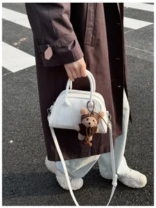 Detailansicht einer weißen Leder-Baguette-Tasche mit einem braunen Plüschbären-Anhänger