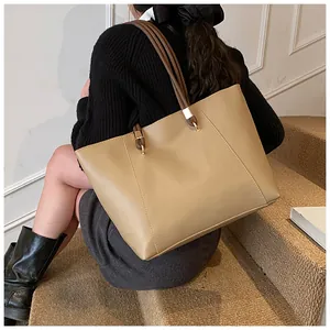 Close-up of khaki tote bag with brown handles and gold hardware on a model