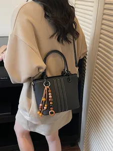 Chic black bucket bag with contrast stitching and ethnic bead charm for women