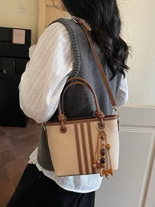Minimalist beige canvas bucket bag with brown leather trim and retro beaded tassel