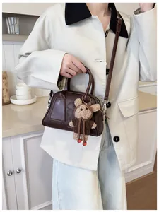 Detail einer braunen Leder-Baguette-Tasche mit süßem Bärenanhänger und Markenlogo