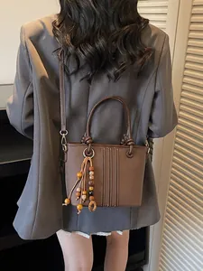 Brown leather bucket bag with wooden bead charm and stitching, elegant crossbody style
