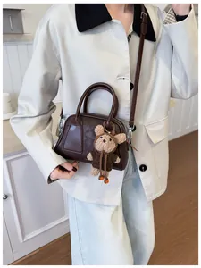 Detail der dunkelbraunen Baguette-Tasche mit glatter Textur und süßem Teddybär-Anhänger