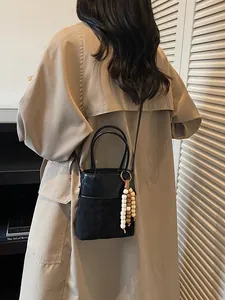 Chic black bucket bag with wood bead tassel shown with a beige trench coat for women
