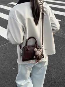 Minimalistische dunkelbraune Leder-Baguette-Tasche mit Bärenanhänger vor Straßenkulisse