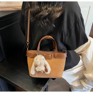 Détail du sac seau en daim marron avec boucle en cuir et pendentif lapin en peluche