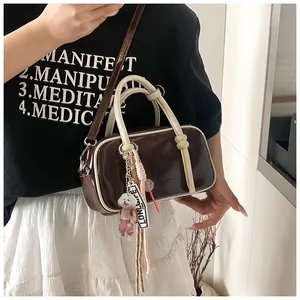 Détail du sac Boston marron avec poignées contrastées et charm chien en peluche