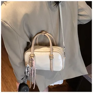 Détail d'un sac Boston beige porté sur un blazer gris-vert avec étiquette décorative