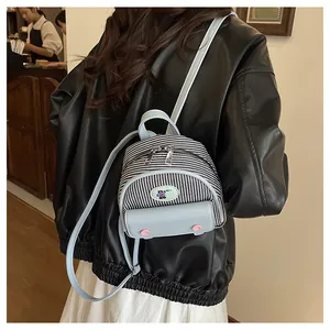 Détail du mini sac à dos rayé avec des lanières en cuir bleu clair portées par le modèle