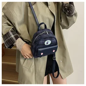 Détail d'un mini sac à dos à carreaux bleus avec écusson ours et trench kaki