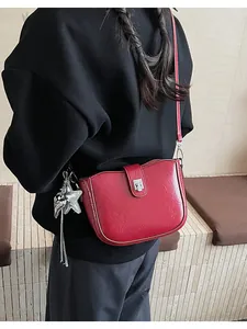 Detail of red crossbody bag with silver star charm and metallic turn-lock closure