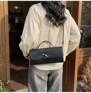 Detail einer eleganten schwarzen Baguette-Tasche mit T-Verschluss und Krokodil-Prägung