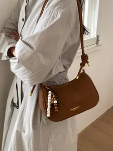 Sac baguette en daim marron avec pendentif en perles porté par le mannequin