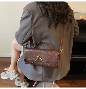 Detailansicht einer dunkelbraunen Baguette-Tasche mit Krokoprägung und Goldschnallenverschluss