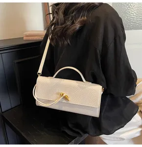 Detailansicht einer weißen Baguette-Tasche mit Schlangenmuster und goldenem Knotenverschluss