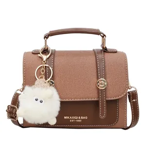 Brown patchwork saddle bag with gold metal buckle and a white plush charm