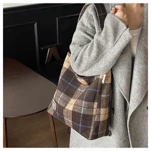 Detail of plaid canvas tote bag with brand label worn with grey coat in cafe setting