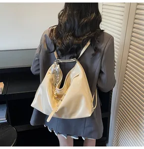 Detail of a shiny cream hobo tote bag with silver bow charm on a person's shoulder