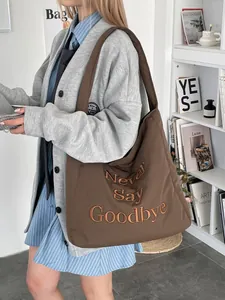 Sac cabas en toile marron avec broderie 'Never Say Goodbye' porté à l'épaule par un mannequin