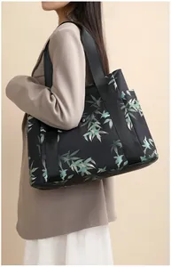 Detail view of the black tote bag showing green leaf patterns and nylon straps on a shoulder