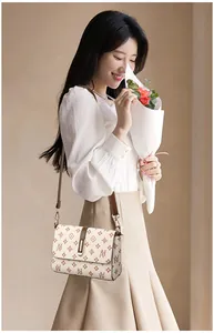 Chique crème crossbodytas met vintage monogrampatroon getoond door een model