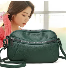 Detail shot of a dark green pebble leather crossbody bag on a model in a bright room