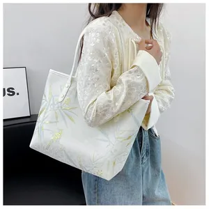 Detail of white tote bag with gold bamboo leaf pattern and bird prints shown on shoulder