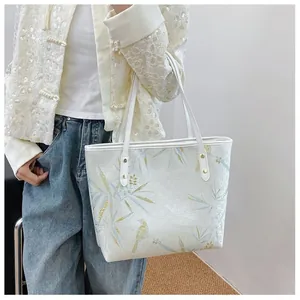Detail of white tote bag with light blue bamboo leaves and golden bird prints