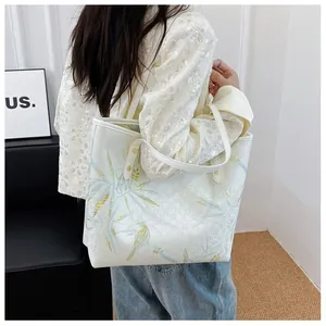 Detail of white tote bag featuring golden bird embroidery and reinforced shoulder straps
