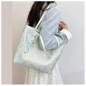 Detail view of large tote bag with blue leaf patterns on model in light blue jacket