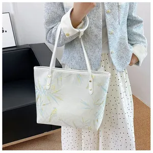 Detail of white tote bag featuring blue bamboo prints and gold bird patterns on the side