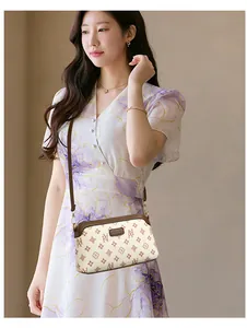 Detail of beige patterned crossbody bag with brown leather trim worn by female model