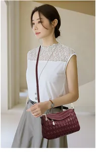 Detail of burgundy quilted crossbody bag with golden zippers worn on shoulder