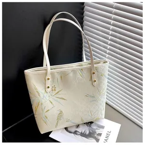 Detail of bamboo and bird embroidery on cream tote bag with gold metal rivets