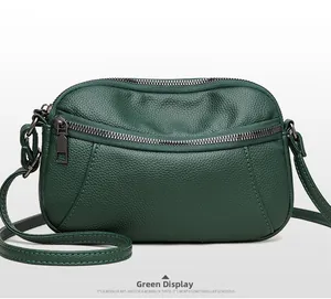 Detail of green leather crossbody bag with lychee texture and gun-metal zippers