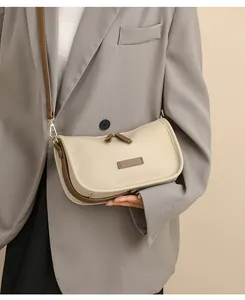 Detail of a beige pebbled leather shoulder bag with brown straps on a grey blazer suit