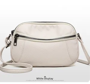 Detail view of cream leather crossbody bag with three zipper compartments and grainy texture