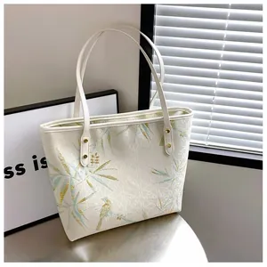 Detailed embroidery of blue birds and bamboo leaves on a cream commuter tote bag
