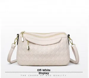 Detail view of beige crossbody bag showing multi-layer zippers and textured rhombus pattern
