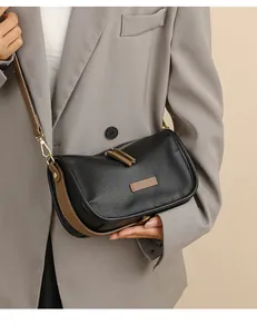 Detail of black lychee texture crossbody bag with brown trim on a gray blazer