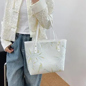 Detail of a white tote bag with bamboo and bird prints, featuring dual shoulder straps