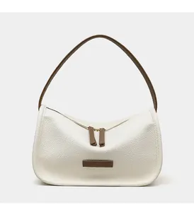 Close-up of litchi grain leather texture and brown strap on ivory white baguette bag