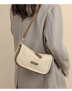 Side view of cream leather shoulder bag with brown trim on a model in gray blazer