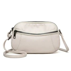 Minimalist cream leather crossbody bag with pebble grain texture and dual zipper pockets