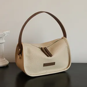Minimalist cream shoulder bag with brown leather handles and half-moon silhouette