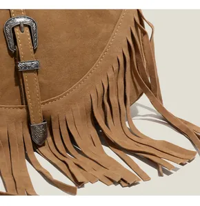 Détail du sac bandoulière en daim marron avec de longues franges et boucle en métal gravée
