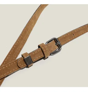 Détail d'une bandoulière en daim marron avec boucle en métal noir et coutures jaunes